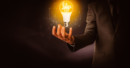 Idea Glowing Bulb In Business Man Hand with Dark Abstract Background. Futuristic and business concept backdrop