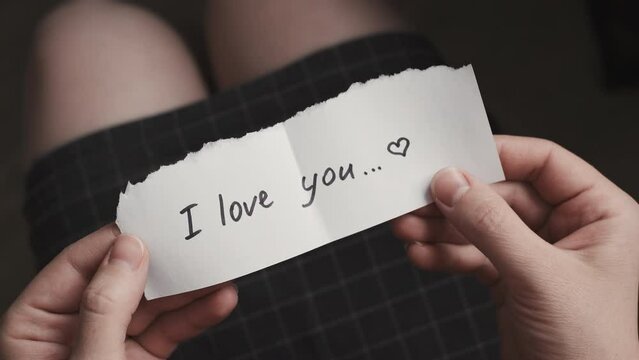 top view of woman in plaid clothes holding paper message with i love you text. Opens a folded sheet, reads and crumples the message. Throw away the message