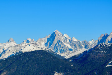 Fototapeta na wymiar The Aiguille Verte surrounded by the snowy forests in Europe, France, Rhone Alpes, Savoie, Alps, in winter on a sunny day.