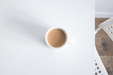 Fototapeta na wymiar White cup on a white table under natural light. Top view flat lay.