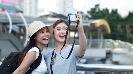 Two Asian female tourists using compact camera to take selfie during city tour.