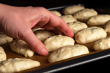 A woman's hand lays the dough before baking, coats it with butter on a baking sheet in a hot oven.