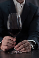 Man in a white shirt and dark suit holds a glass of wine on the bar
