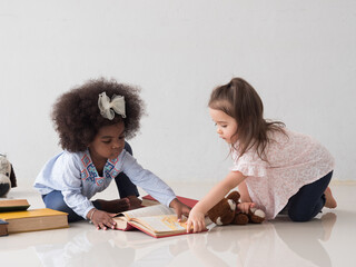 Cute little African and Caucasian girls are reading pile of books together. Diversity, Back to School  and Education