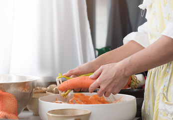 Close up, hand using peeler peeling the carrot skin. Housewife preparing ingredient to cook.