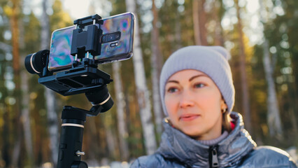 Woman Holding On Handheld Film 3-axis Gimbal Stabilization Device in Winter for Smartphone. Girl Blogger Make Selfie, Broadcast Video Blogging, Vlogging. Videographer Operator Take Photo Video.