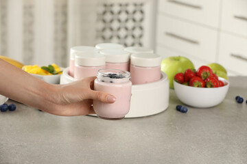 Woman holding jar of yogurt with blueberry over light grey table, closeup