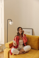 Portrait of young stylish woman sitting cross-legged on sofa at home with closed eyes. Girl wearing...