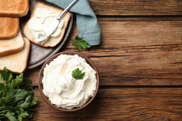 Obraz na płótnie Canvas Toasted bread and delicious cream cheese with parsley on wooden table, flat lay. Space for text