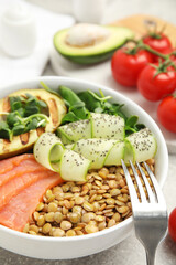 Delicious lentil bowl with salmon, avocado and cucumber on grey table