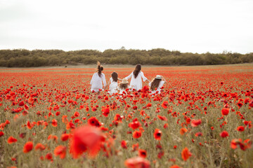 Beautiful mother and daughters in white dresses run through the poppy field