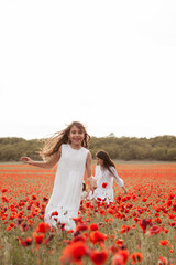 Beautiful mother and daughters in white dresses run through the poppy field