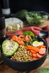 Delicious lentil bowl with carrot, avocado, egg and salmon on wooden table