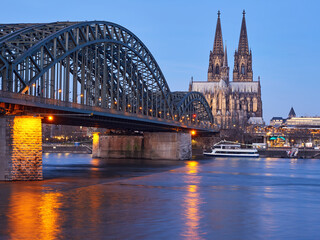 The beautifully illuminated cathedral in the German city of Cologne and the Hohenzollern Bridge over the river Rhine at dawn.
