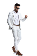 attractive young man with sunglasses holding hand in pocket and walking