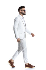 side view of cool young guy in white suit wearing glasses and walking