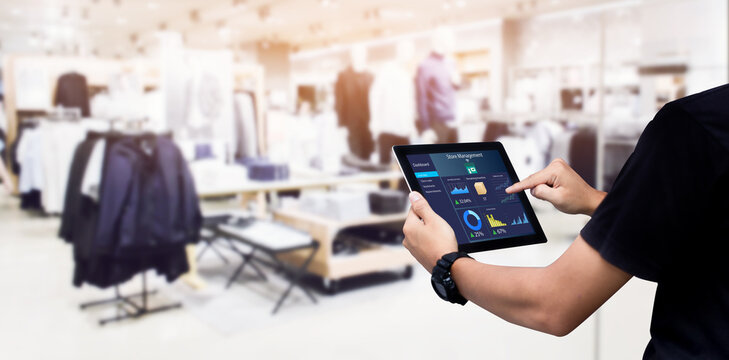Smart store management systems concept.Manager using digital tablet on blurred clothing store as background