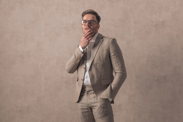 confident businessman with glasses holding hand in pocket and touching chin