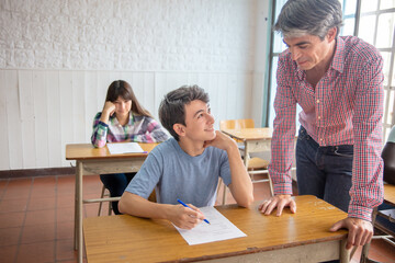 Group of multi ethnic high school students having test at classroom, teacher supervising.