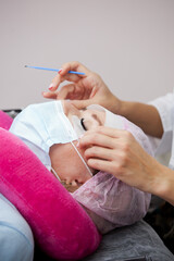 A girl makes the procedure for extending eyelashes during a pandemic, a master with tools in her hands