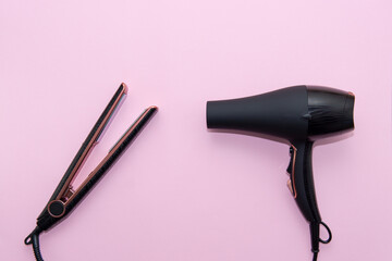 Top view of black hair straightening iron and a hairdryer on pink background. Hair care concept