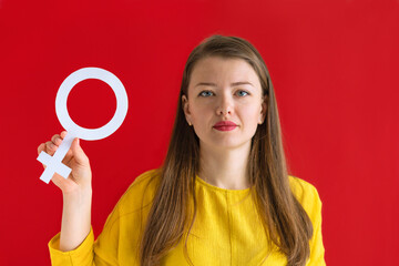 young  woman with feminine sign on red background. fight against injustice, struggle for gender equality, confrontation, independence. international womens day 8 march. concept of feminism, power
