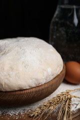 Fototapeta na wymiar Dough in wooden bowl against black background. Sodawater bread recipe