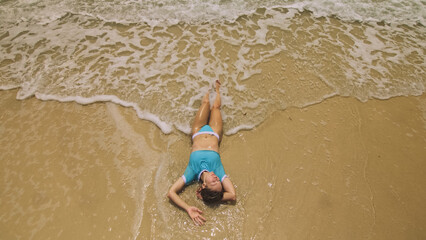 Fototapeta na wymiar Crazy madwoman daring funny woman lying on shallow water sea. Top view happy slightly tipsy woman enjoying her vacation on a tropical island. Smiling girl funny posing. Concept summer holidays