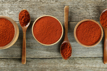 Bowls and spoons of paprika on wooden table, flat lay