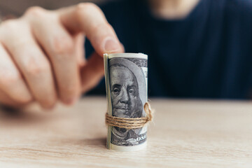 The person points to a rolled stack of dollar bills. The concept of the first earned money