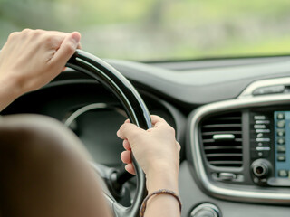 Female hands on the black glossy steering wheel of a car.. Driving a car. Soft focus