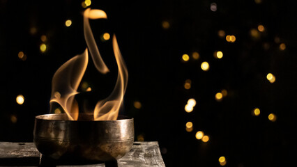 Beautiful bokeh of a flaming singing bowl, on black and gold background © Natura