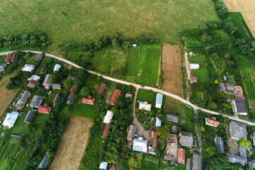 Aerial landscape view of village houses and distant green cultivated agricultural fields with growing crops on bright summer day