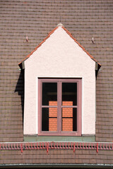 Portrait close-up of a roof with brown tiles in Germany with a skylight. Through the skylight you can see the tiles from the roof behind.