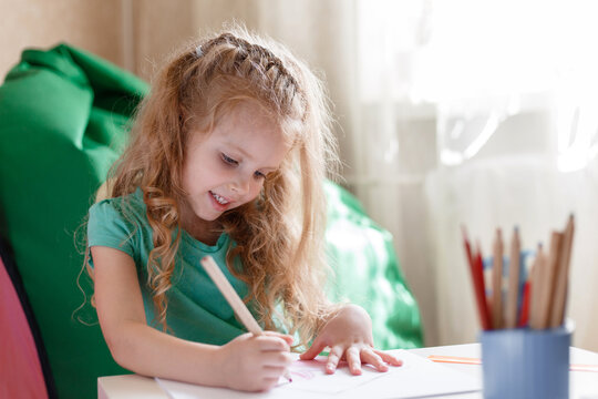 Little girl child kid in children's room play draws with interest by pencils in nursery. 5 Years happy smiling preschool baby girl draws in room alone at home or Kindergarten
