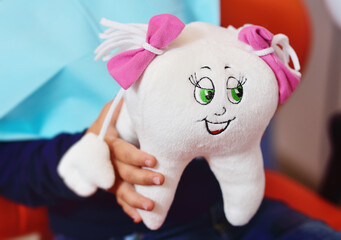 close-up of a child in an orange dental chair holding a stuffed toy in the shape of a large tooth with eyes and a smile.