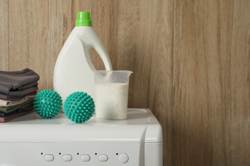 Dryer balls, stacked clean clothes and detergents on washing machine. Space for text