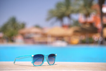 Closeup of blue sunglasses on swimming pool side at tropical resort on warm sunny day. Summer vacation concept