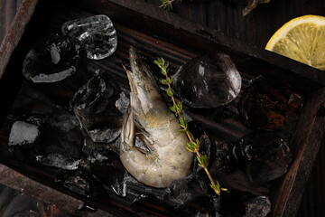 Frozen shrimp, prawn with ice cubes and lemon in a wooden box.