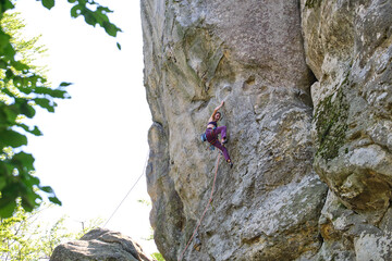 Determined girl climber clambering up steep wall of rocky mountain. Sportswoman overcoming difficult route. Engaging in extreme sports and rock climbing hobby concept