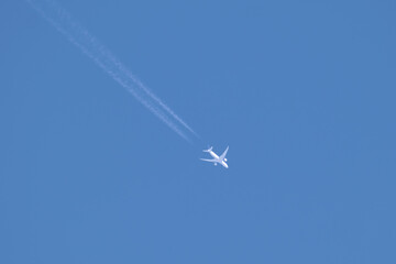 Distant passenger jet plane flying on high altitude on clear blue sky leaving white smoke trace of contrail behind. Air transportation concept