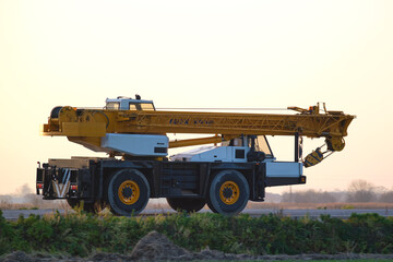 Heavy duty mobile lifting crane driving on intercity road at sunset