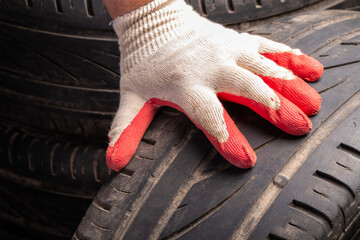 Hand in a working glove touching old used tire surface with wear indicator.