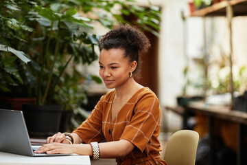 Happy young owner of modern orangerie or greenhouse sitting in front of laptop while looking through design trends online