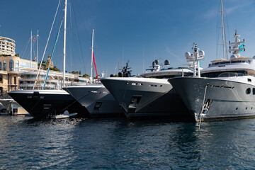 Fototapeta na wymiar A lot of huge yachts are in port of Monaco at sunny day, Monte Carlo, mountain is on background, glossy board of the motor boat, megayachts are moored in marina, sun reflection on glossy board