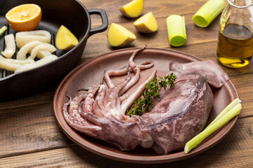 Fresh squid with tentacles on plate. Chopped squid rings and lemon in frying pan.