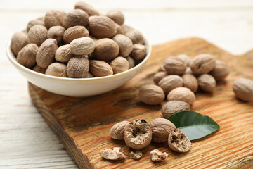Nutmeg seeds and green leaf on white wooden table, closeup