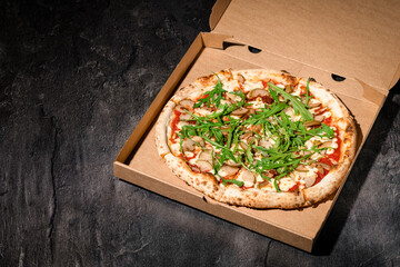 Pizza in paper box on black stone background. Italian traditional food. Delicious pizza with pear, parmigiano-reggiano cheese and rucola. Restaurant menu, food delivery and take-out. Copy space