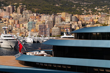 Landmarks of Monaco through decks of huge yacht of blue color in port Hercules at sunny day, glossy board of the motor boat, sun reflection on glossy board, mountains are on background