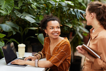 Two pretty intercultural girls discussing which sorts of flowers to order in online shop selling...